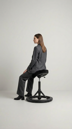 En kvinde i gråt jakkesæt sidder på en ergonomisk sadelstol med rund base mod en lys baggrund.