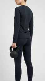 En kvinde i sort træningstøj set bagfra, der holder en kettlebell mod en lys baggrund.