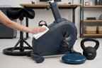 En person rengør en mørkeblå motionscykel med en hvid klud i et kontor ved siden af en kettlebell.