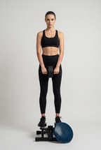 En kvinde i sort træningstøj holder et mavehjul foran sig i et lyst studie med træningsmaskiner.